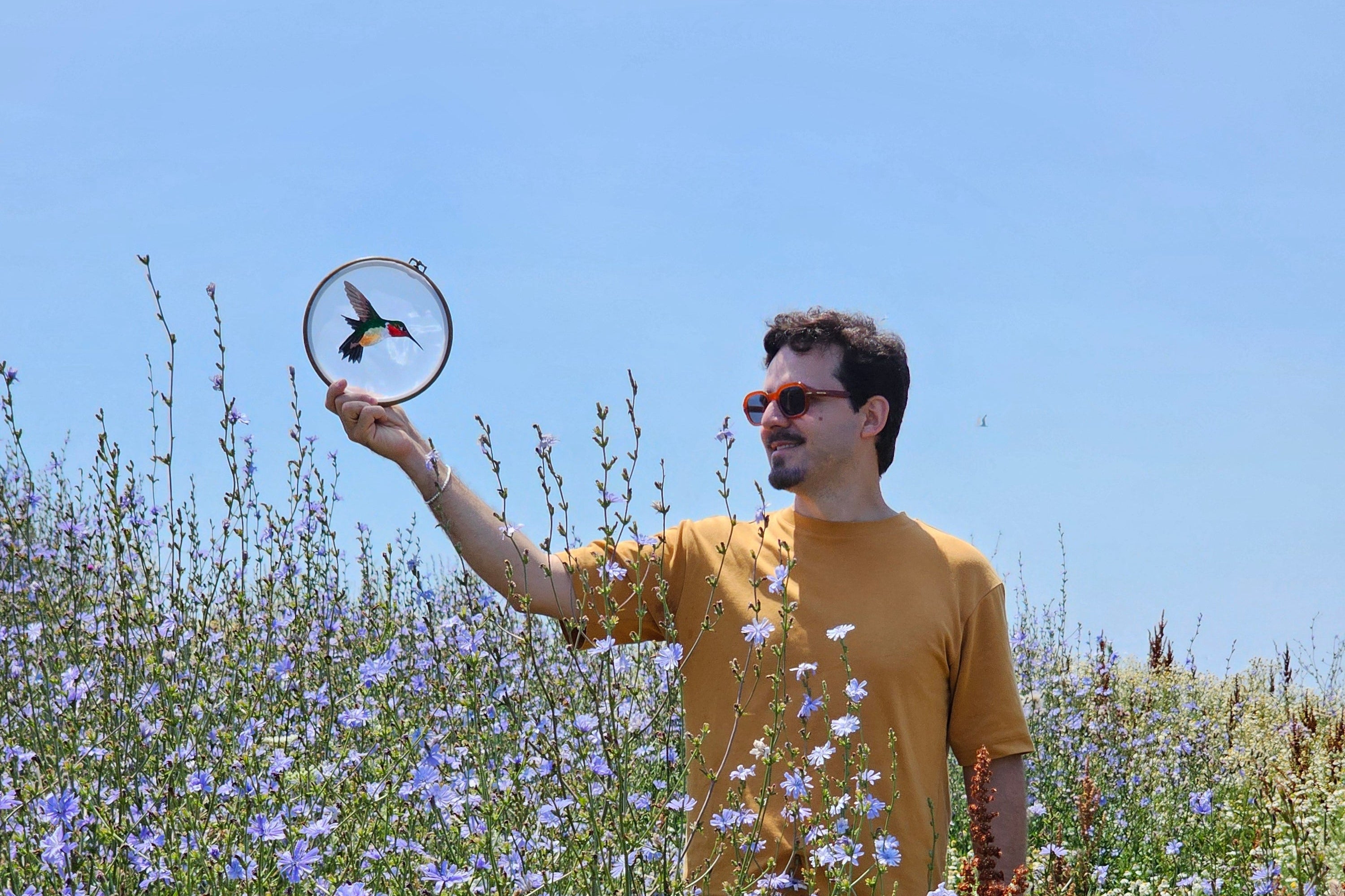 Person in a yellow dress standing in a field of flowers with a clear blue sky.